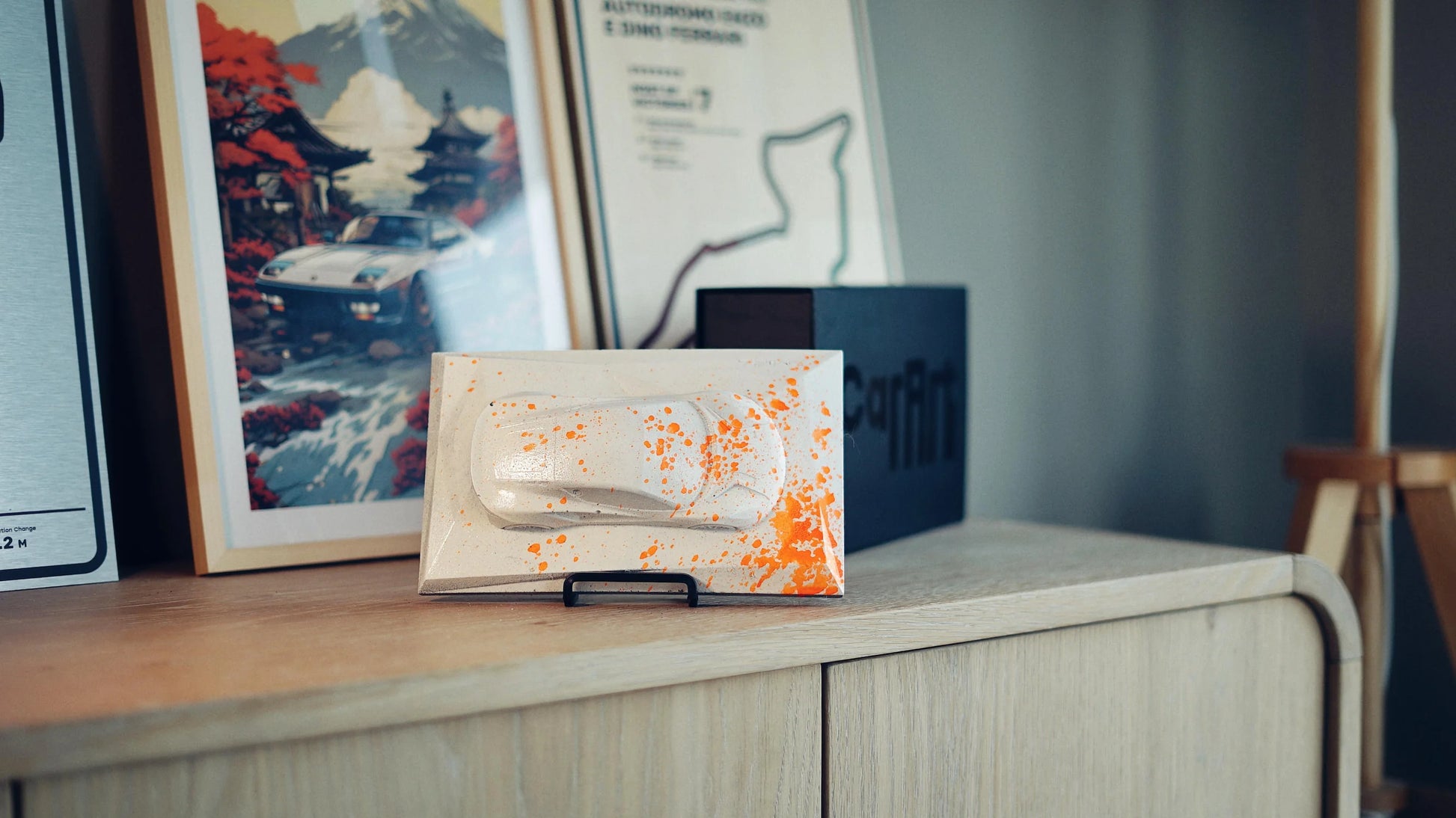 Lotus Emira concrete sculpture mockup in grey with neon orange paint splatter, landscape display by CarArt Dubai